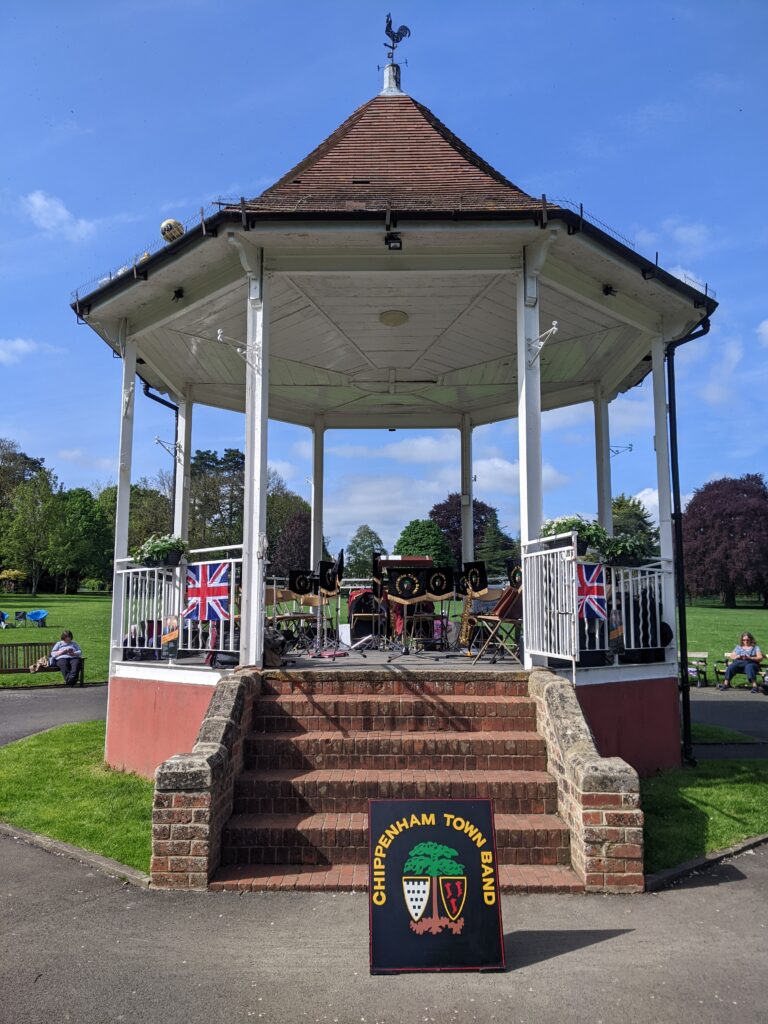 Empty bandstand (during interval) with Chippenham Town Band board in front and music stands present.